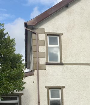 Close-up of a rendered building exterior with sash windows and guttering