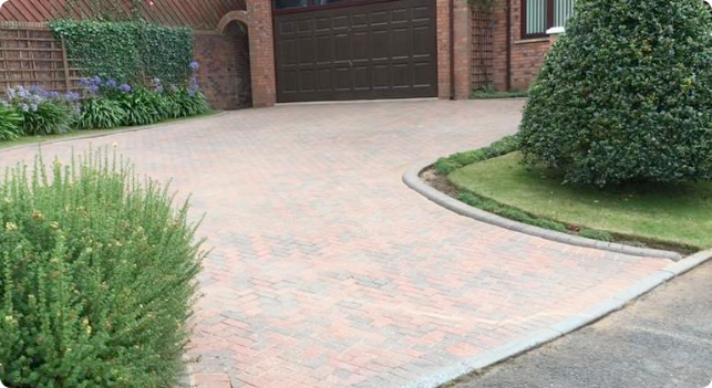 Clean block paved driveway leading to a brick house with garage door and manicured shrubs